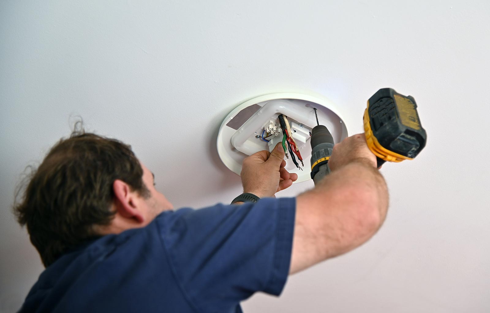Professional electrician drilling a hole for a new ceiling light fixture.